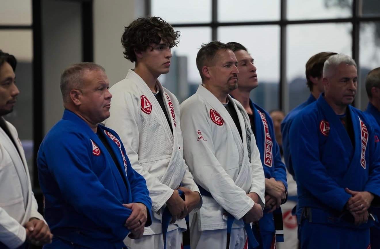 Adult students and coaches in blue and white Gracie Barra gis lined up on the mat