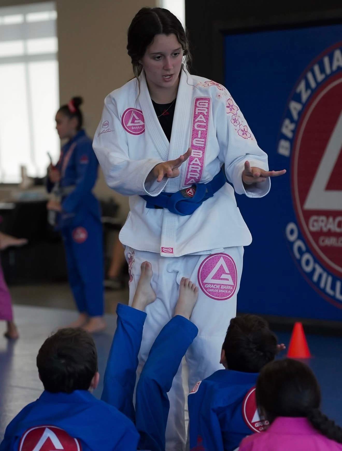 A coach in a white Gracie Barra gi teaches a kids class in front of the Gracie Barra Ocotillo wall banner